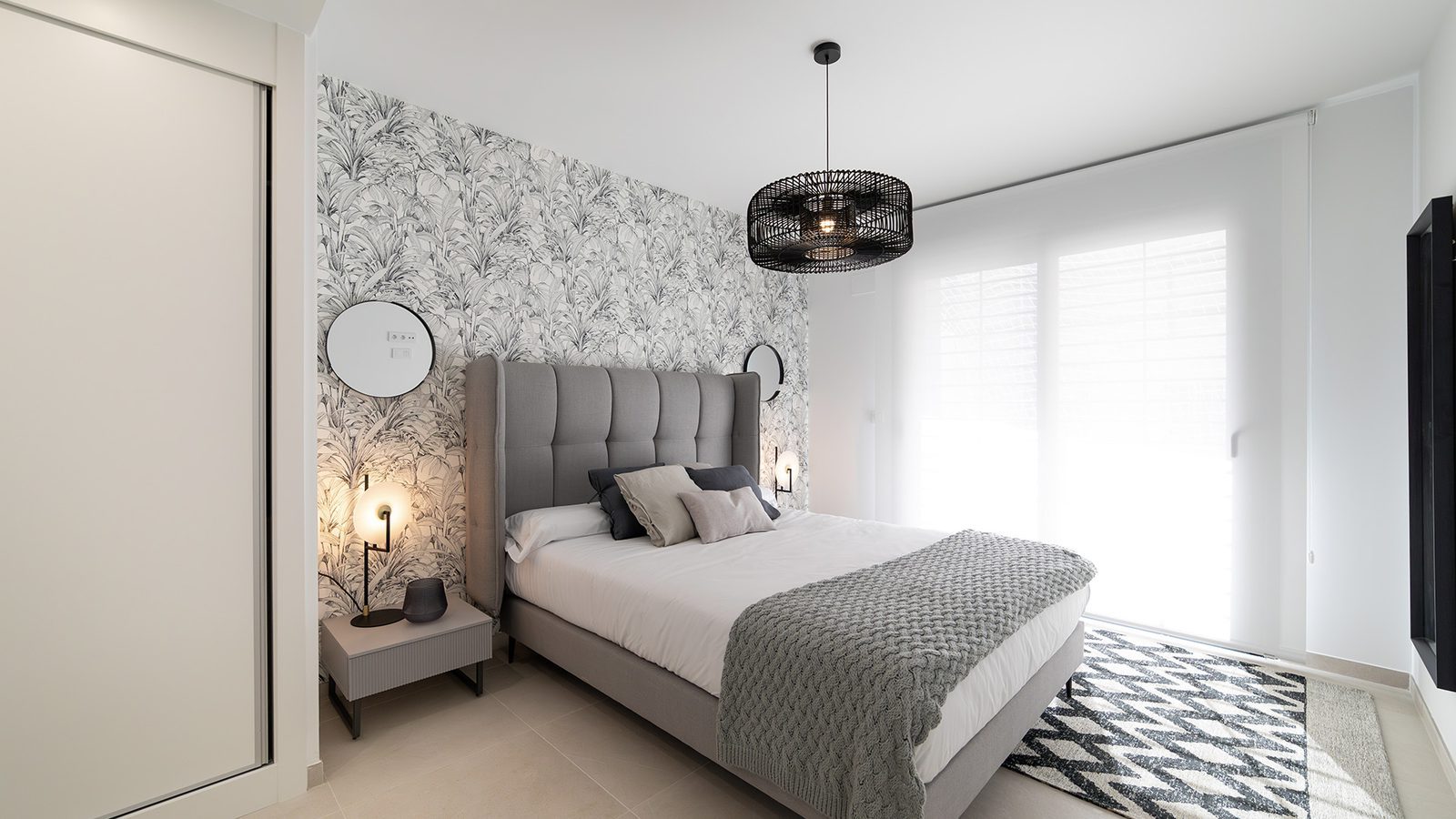 Bright master bedroom with upholstered bed, patterned wallpaper and large window of a