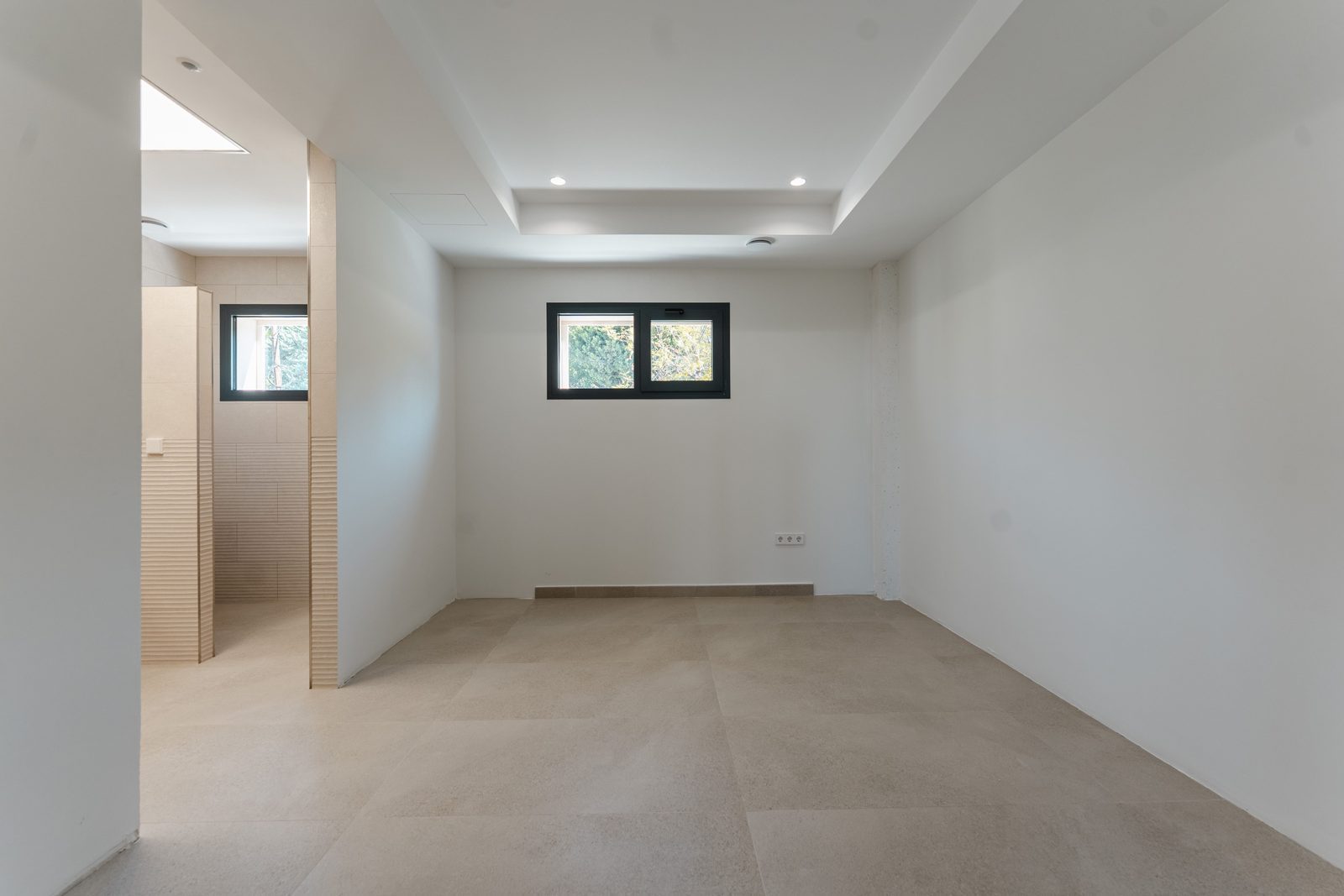 A bright, empty room with tiled floors and a window overlooking greenery in a 5-bedroom villa in Altea - The Estates