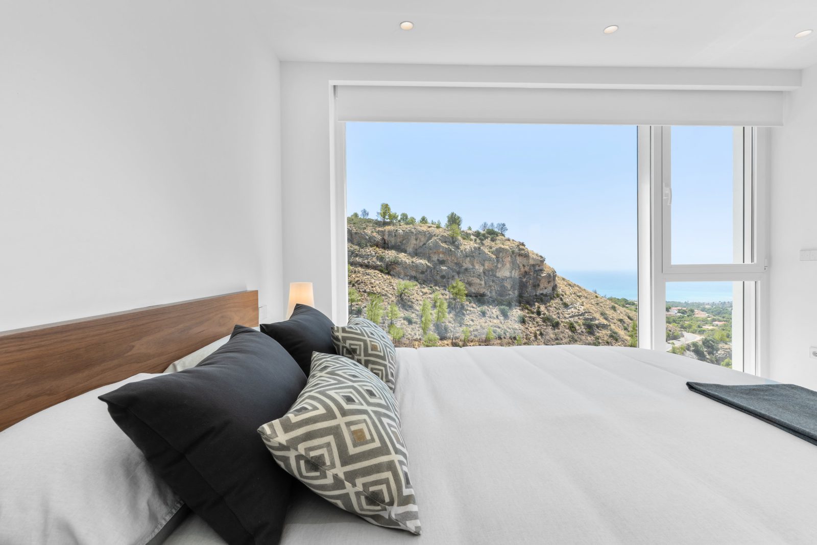 A bright bedroom with a large window showcasing panoramic sea and mountain views of a 4-bedroom villa in Altea - The Estates