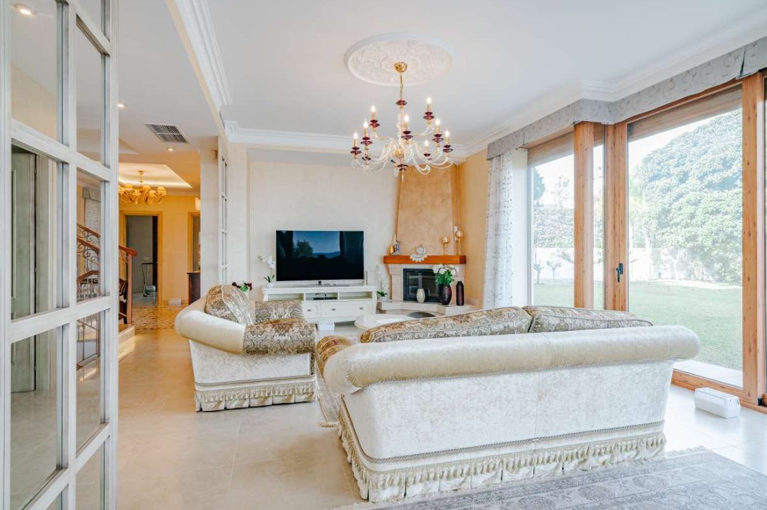 Elegant living room with a chandelier and large windows overlooking a garden in a 6-bedroom villa in Calpe - The Estates