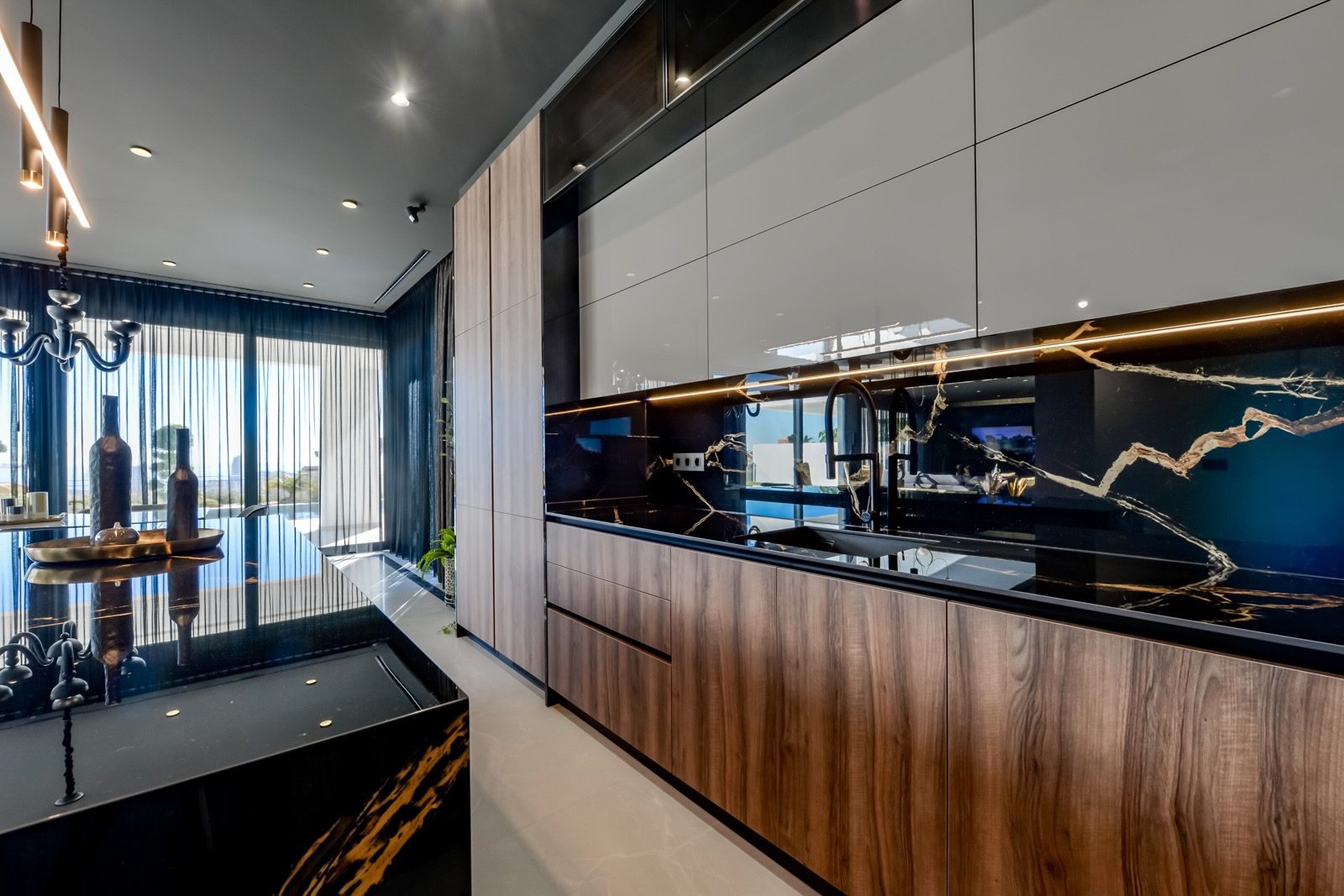 A modern kitchen with sleek cabinetry and a striking mirrored backsplash in a 7-bedroom villa in Finestrat - The Estates
