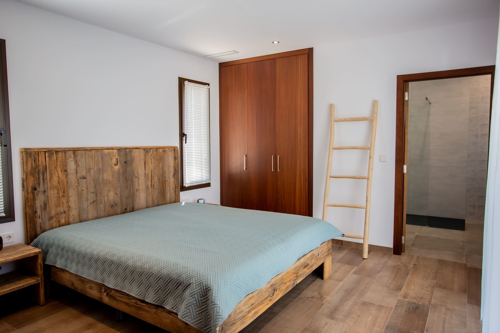 A bedroom with a wooden bed frame and built-in wardrobe in a 3-bedroom villa in Javea - The Estates