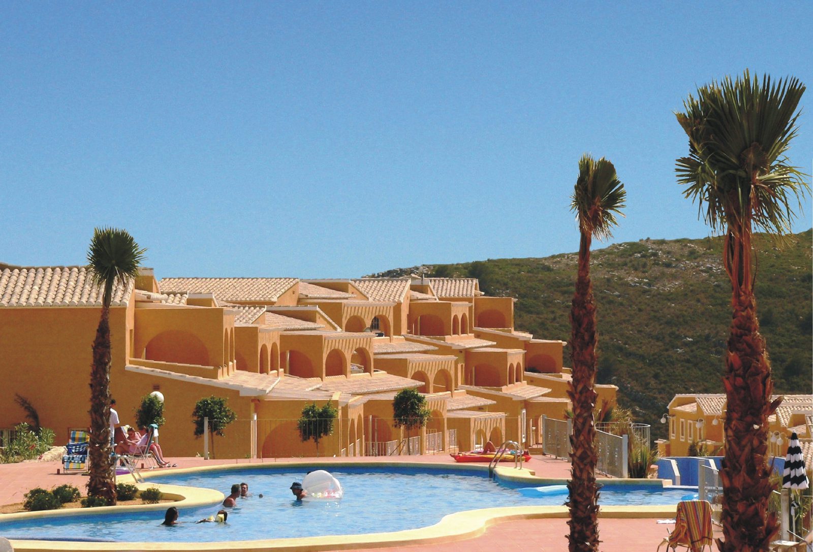 A swimming pool and apartment complex with palm trees in Benitachell - The Estates