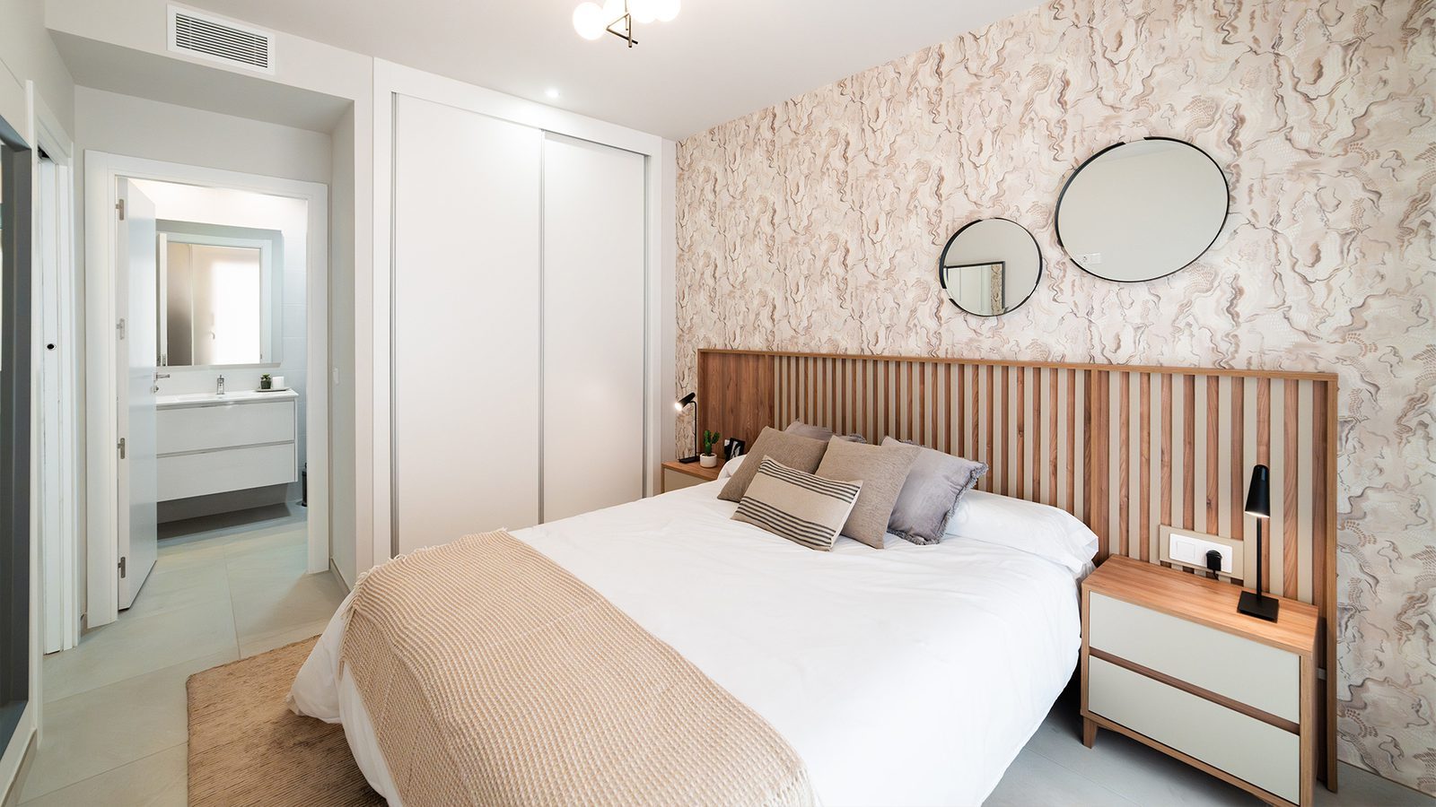 Modern bedroom with king-size bed, patterned feature wall and ensuite bathroom in a 3-bedroom bungalow in Pulpí - The Estates