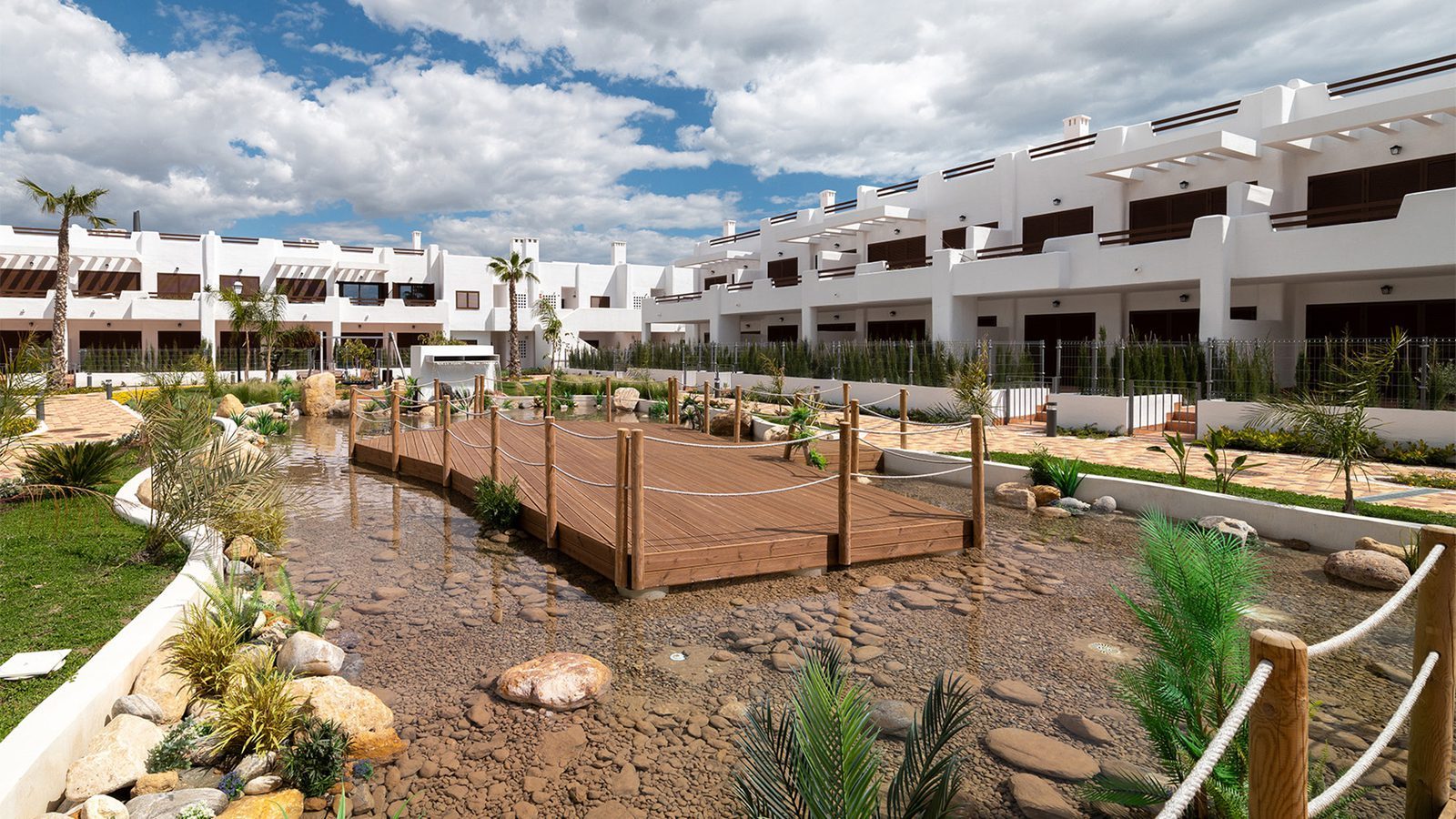 Landscaped courtyard with a rock-lined stream and wooden footbridge at a 2-bedroom bungalow in Pulpí - The Estates