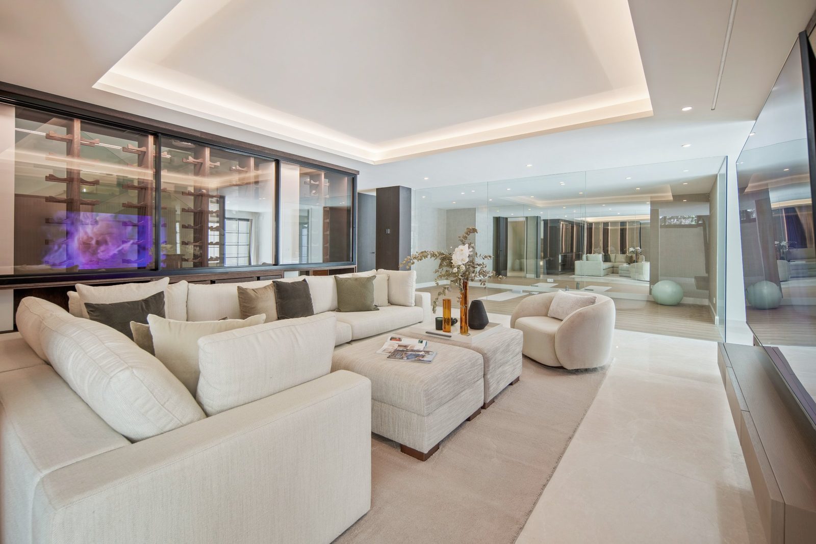 Contemporary living room with cream sectional sofa, TV wall and mirrored interiors in a 6-bedroom villa in Málaga - The Estates