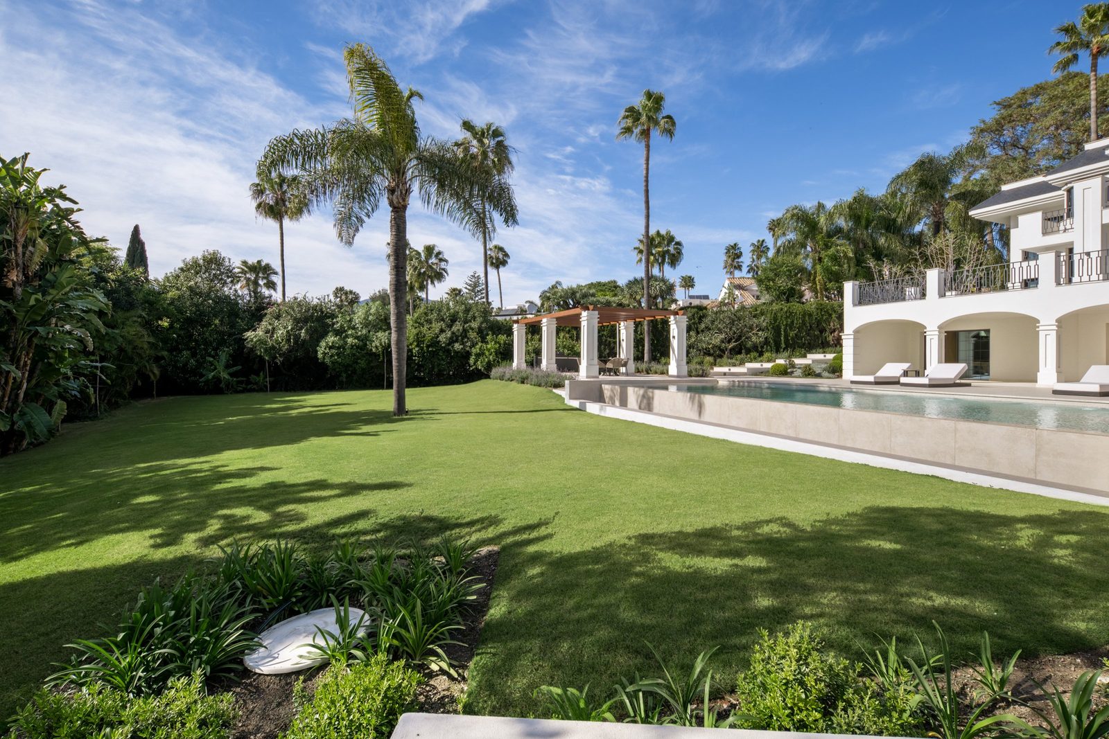 Lush garden with palm trees, pergola and pool of a