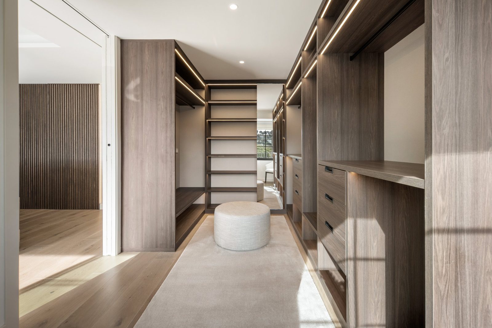 Walk-in dressing room with illuminated wooden wardrobes and central ottoman of a 6-bedroom villa in Málaga - The Estates