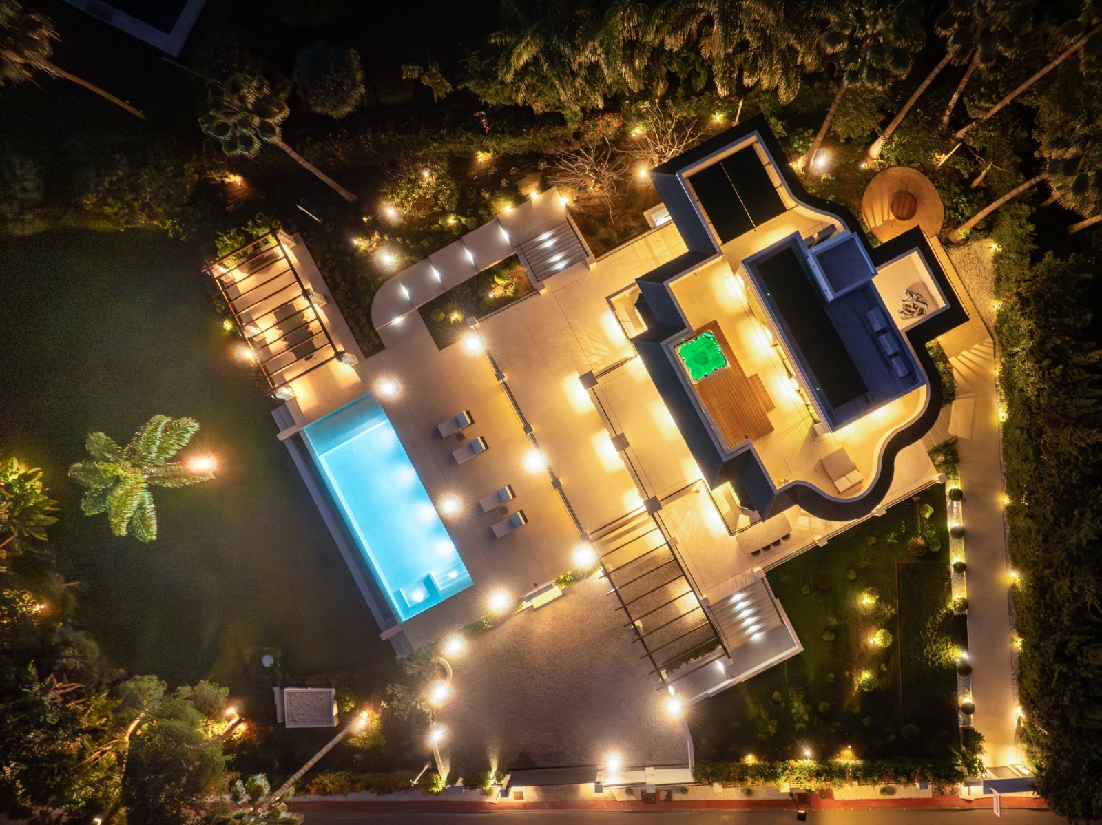 Aerial night view of a luxury villa with illuminated pool, terraces and tropical gardens in Marbella, Málaga - The Estates