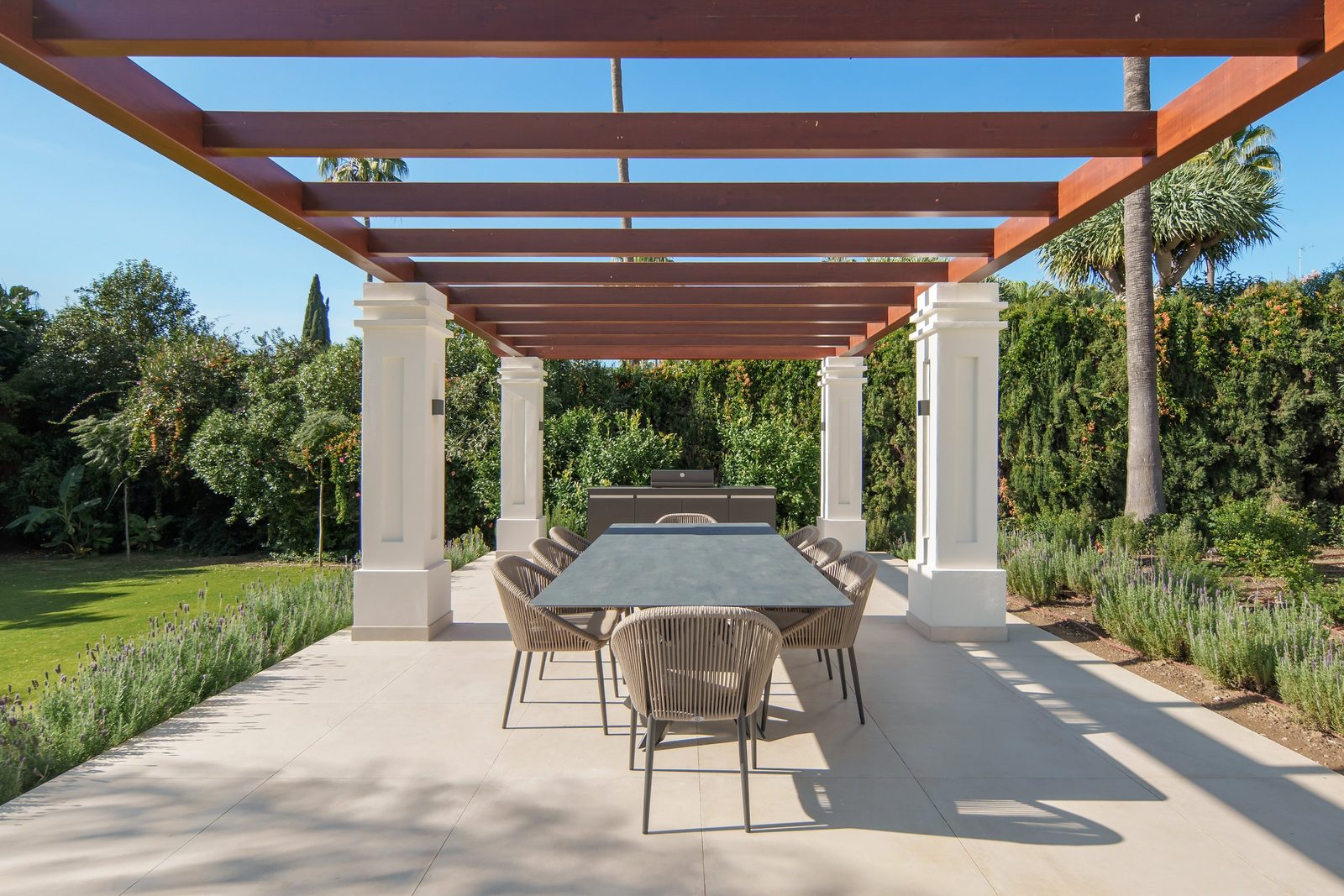 Outdoor dining terrace with pergola, table, chairs and barbecue in the garden of a 6-bedroom villa in Málaga - The Estates