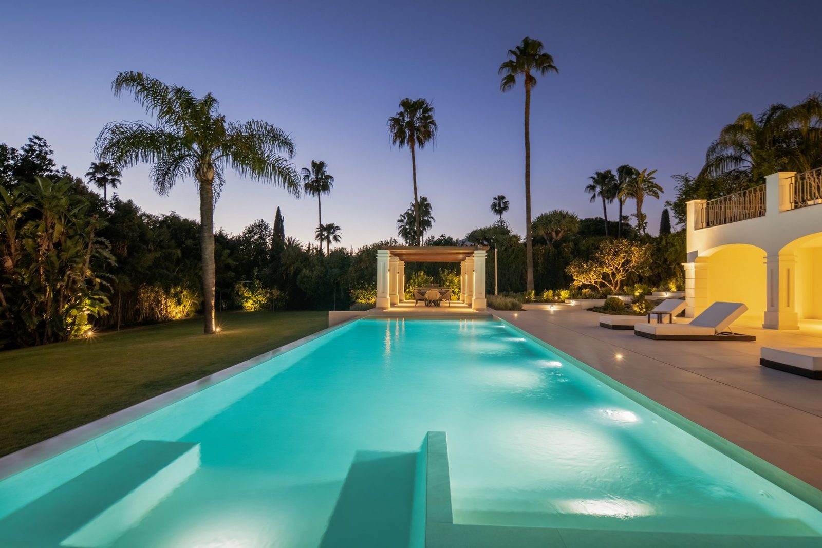 Illuminated swimming pool, landscaped gardens and palm trees at dusk at a
