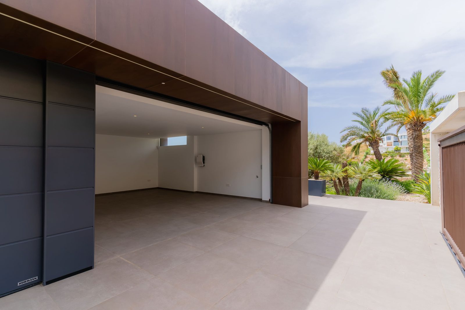 A modern garage with palm trees visible beyond of a 5-bedroom villa in Benitachell - The Estates