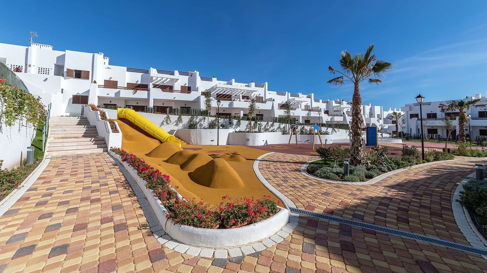 Communal playground and landscaped walkways among white bungalow homes in Pulpí - The Estates