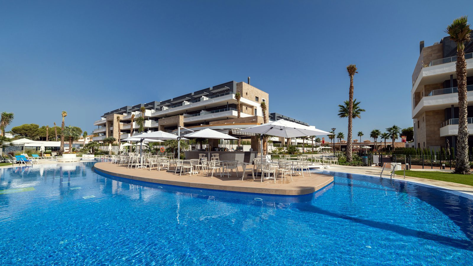 Resort-style complex with a large pool, palm trees and outdoor dining area of a 3-bedroom apartment in Orihuela - The Estates