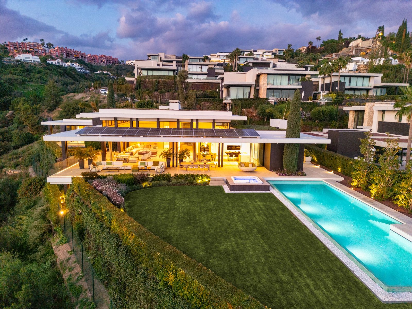 Aerial view of a modern villa with illuminated terraces, landscaped garden and swimming pool in Benahavís, Málaga - The Estates