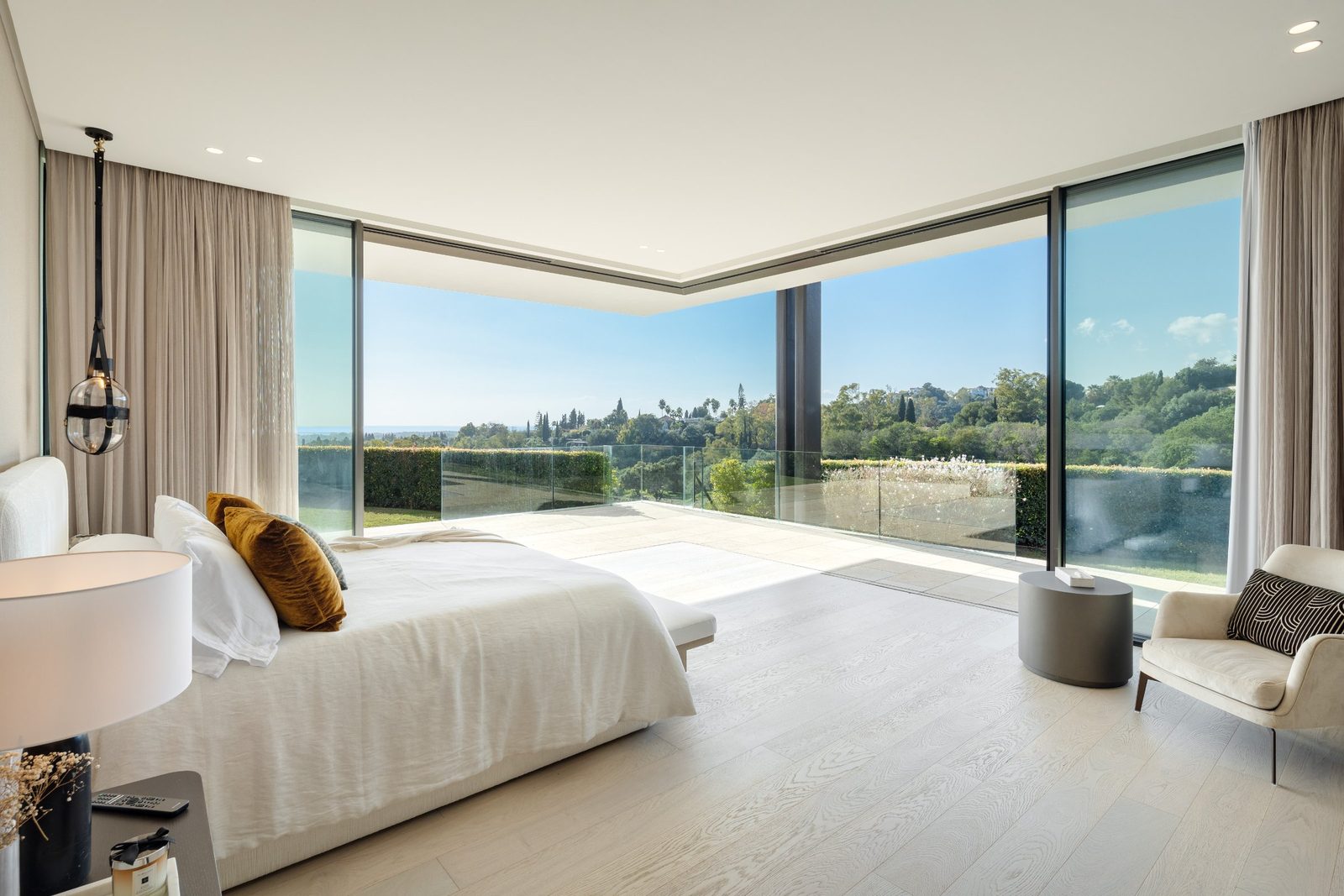 Bright modern bedroom with floor-to-ceiling windows overlooking landscaped gardens and the sea in a 6-bedroom villa in Málaga - The Estates