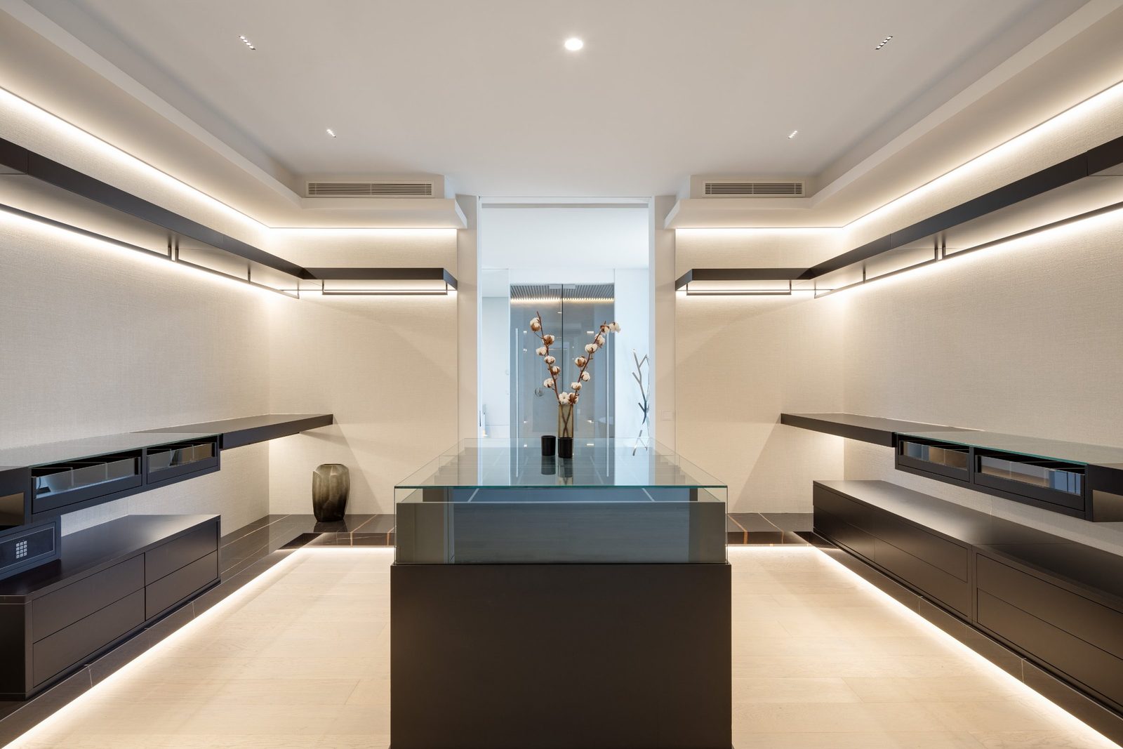 Contemporary walk-in wardrobe with illuminated cabinetry and glass island of a