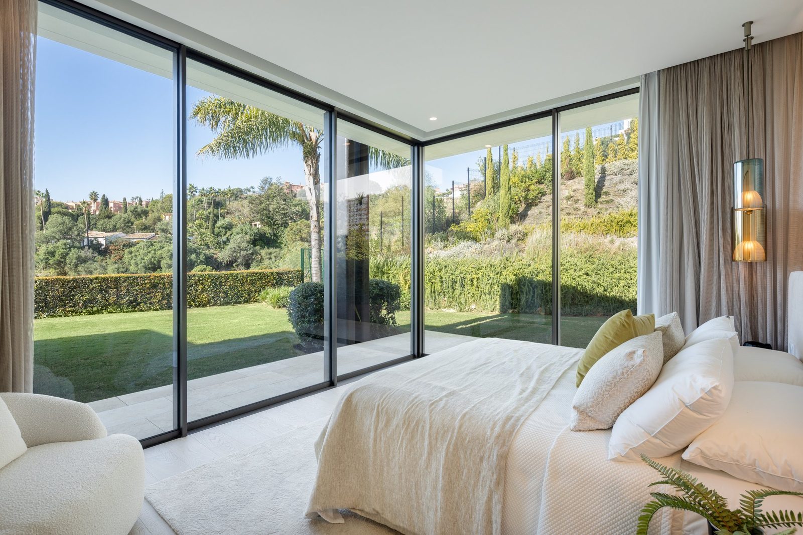 Bright bedroom with floor-to-ceiling windows overlooking a landscaped garden of a 6-bedroom villa in Málaga - The Estates