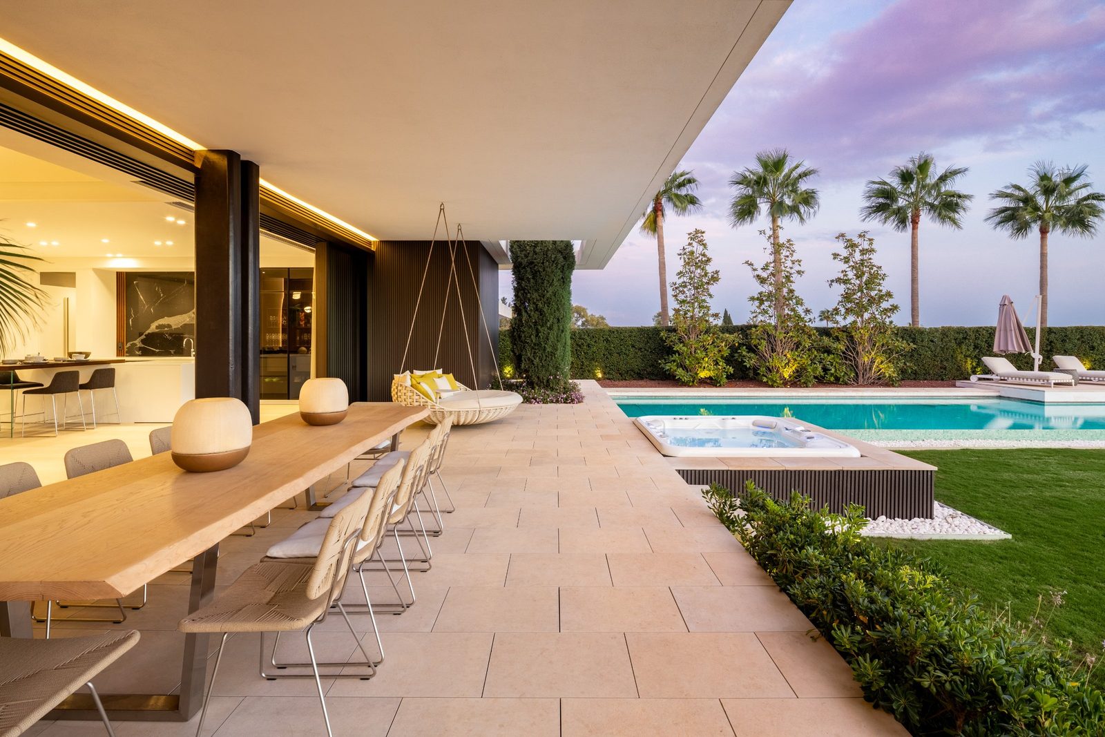 Covered terrace with dining table, swing chair, pool and garden of a 6-bedroom villa in Málaga - The Estates