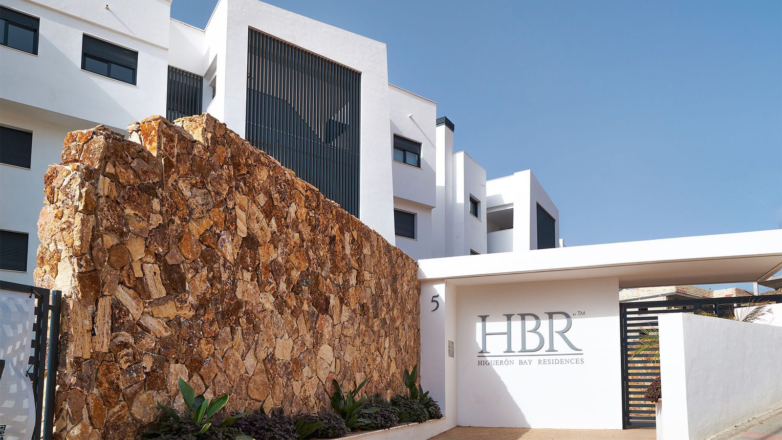 Modern HBR residence entrance with stone wall and white contemporary buildings, of a 2-bedroom penthouse in Fuengirola - The Estates