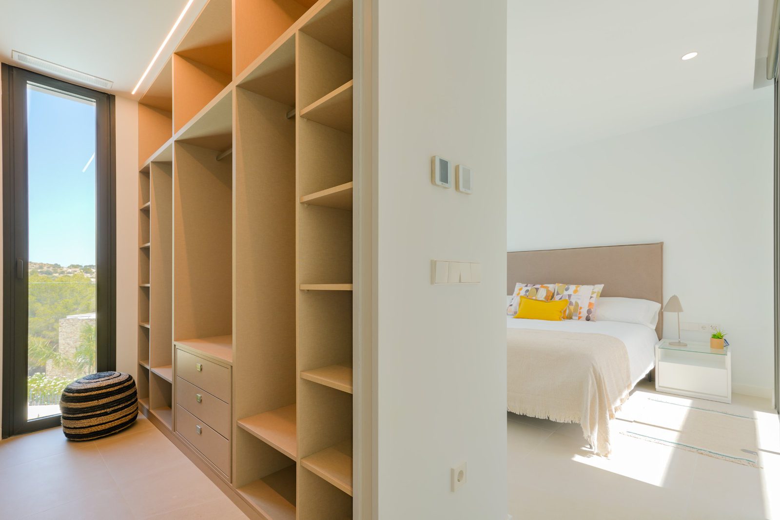 A bright bedroom with built-in wardrobes and a window overlooking countryside in a 4-bedroom villa in Moraira - The Estates