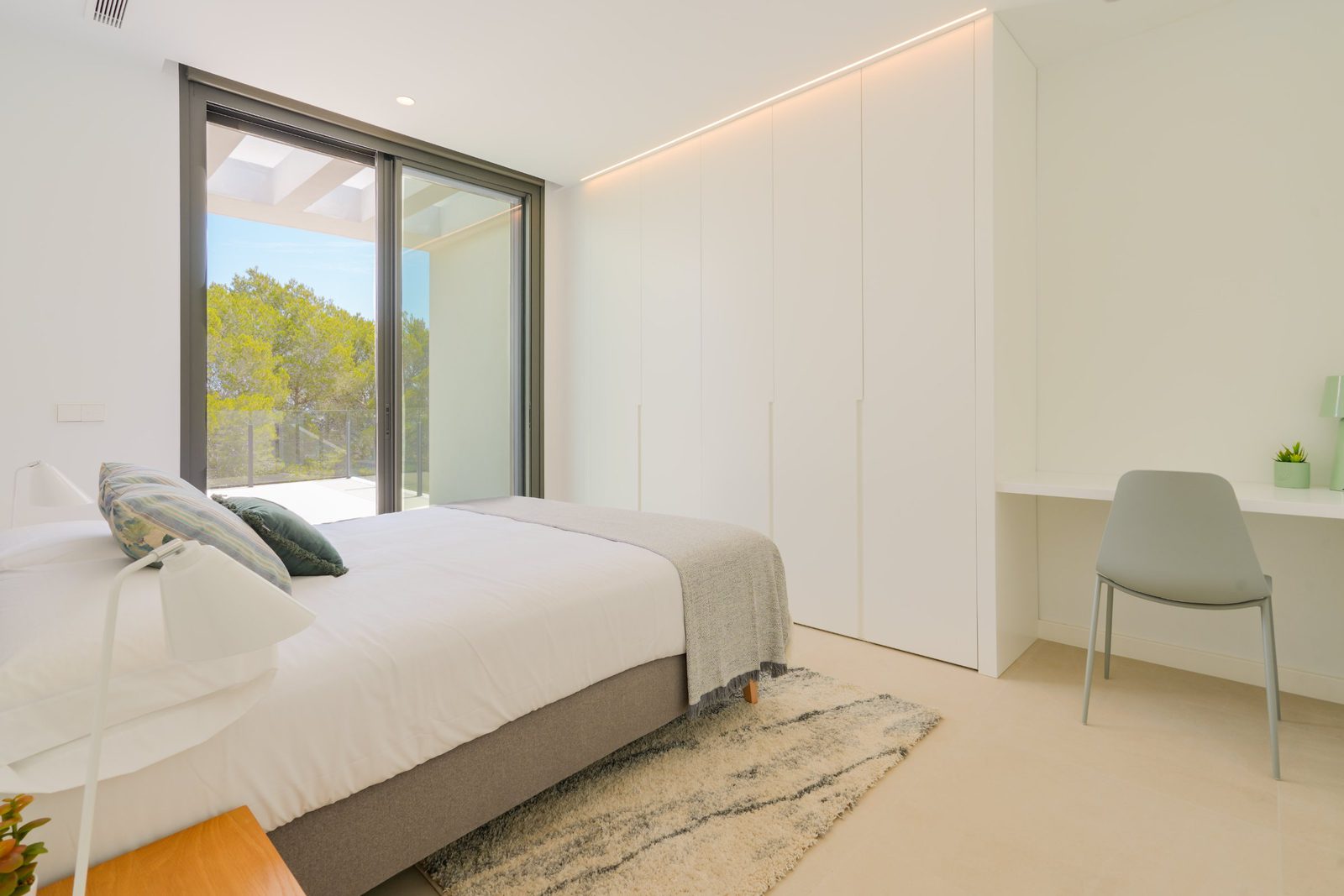 A bright bedroom with built-in wardrobes and a desk, overlooking countryside in a 4-bedroom villa in Moraira - The Estates
