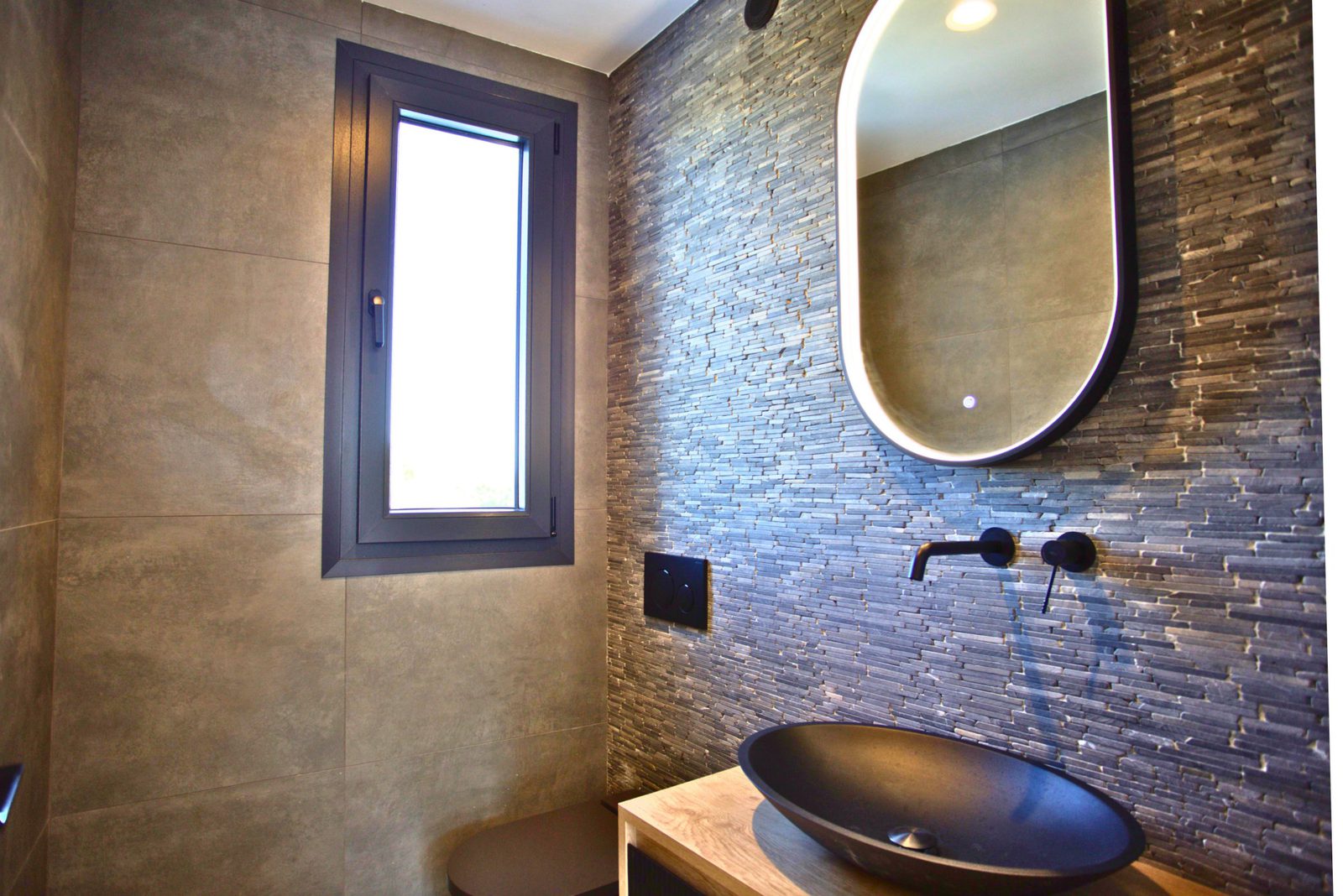 Stylish bathroom interior with stone walls, a modern sink, and a window in a 3-bedroom villa in Moraira - The Estates