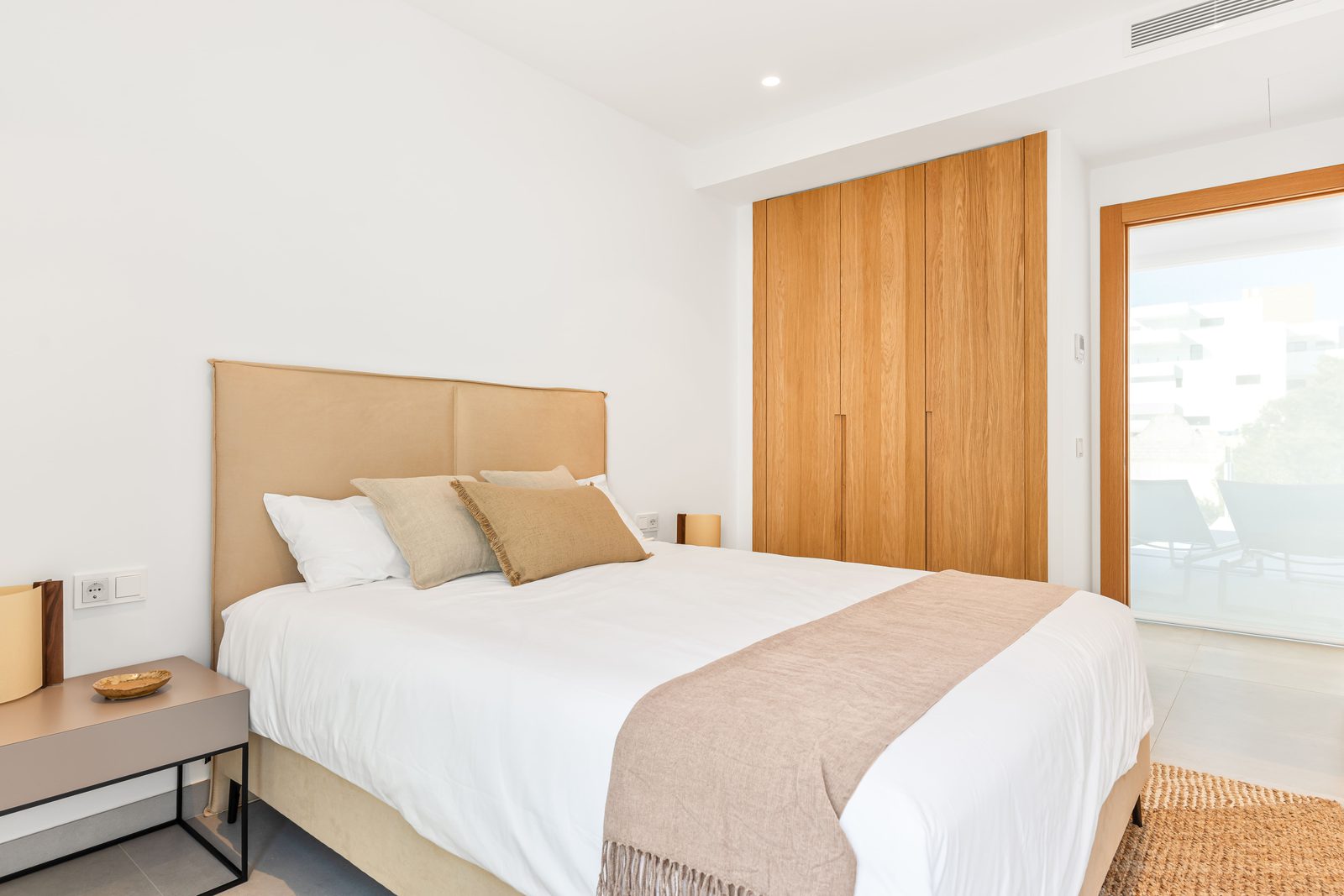 A bright bedroom with wooden wardrobes and a balcony view of a 3-bedroom villa in Benitachell - The Estates