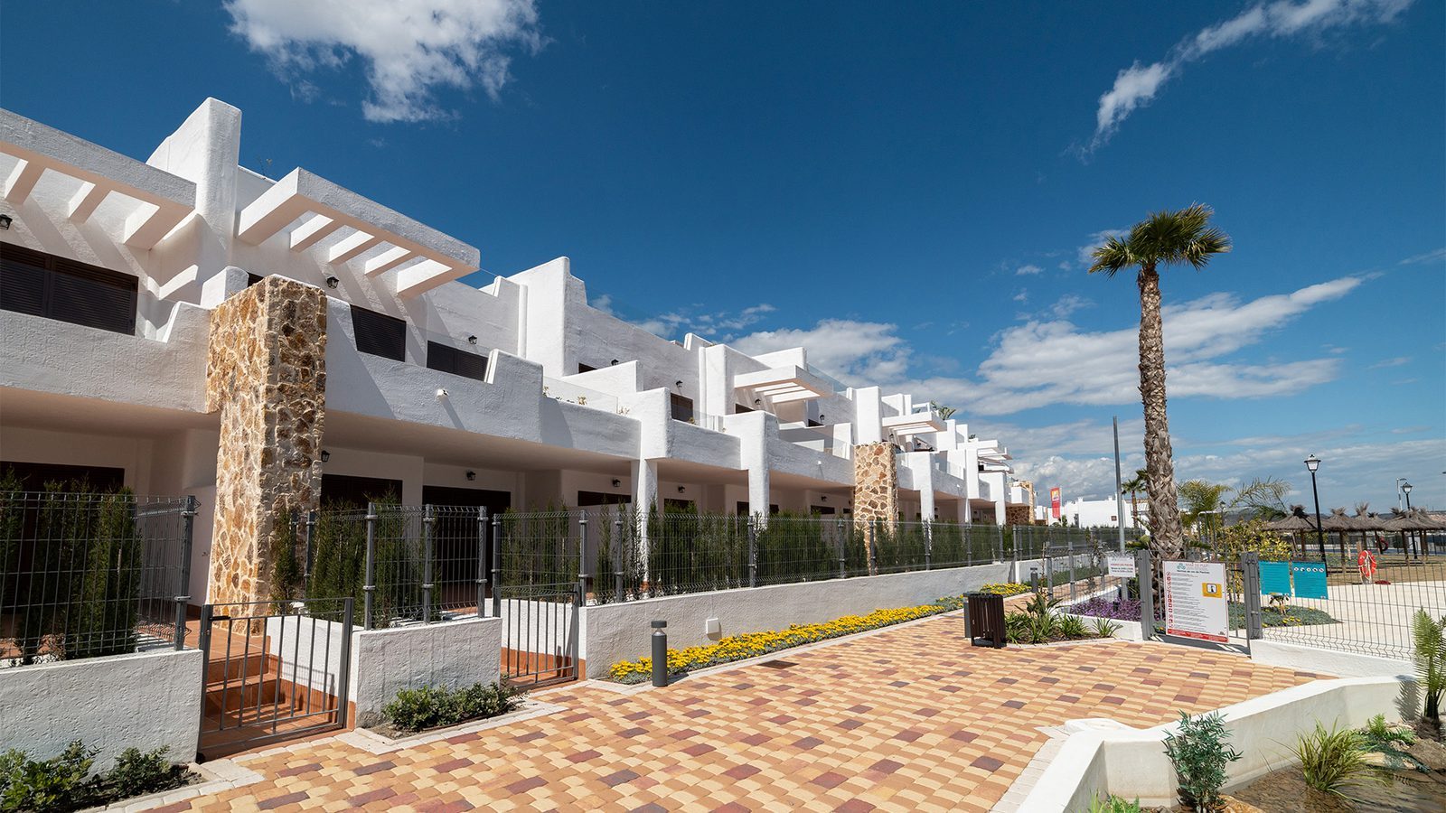 White bungalow exteriors with landscaped walkway and palm trees in Pulpí - The Estates