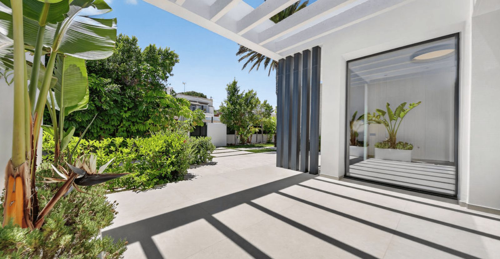 A modern villa entrance with lush greenery and sea views of a 4-bedroom villa in La Nucia - The Estates