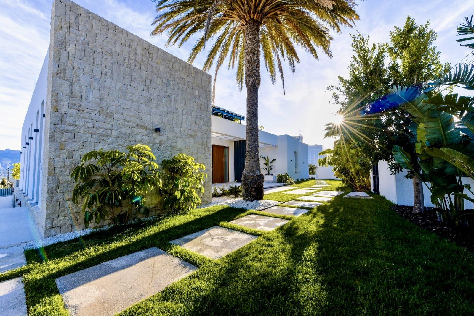 Modern villa exterior with lush landscaping and palm trees, offering sea and city views - The Estates