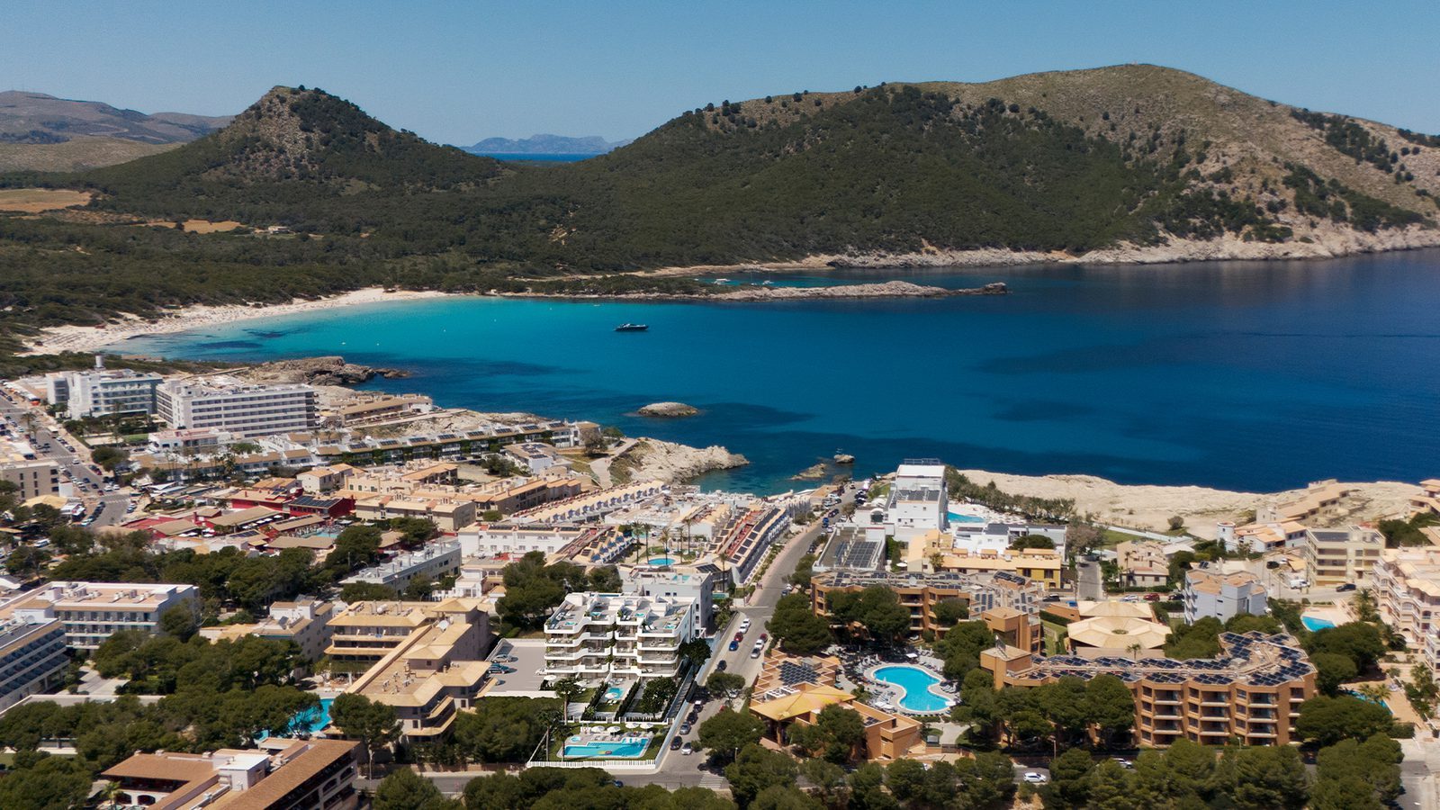 Aerial view of a turquoise bay, coastal resort and hills near a 2-bedroom apartment in Capdepera - The Estates