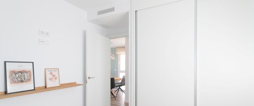 Bright hallway with framed artwork, open door and built-in white wardrobes of a 4-bedroom villa in Finestrat - The Estates