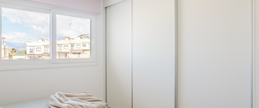 Bright bedroom with built-in wardrobes and mountain views through a window of a 4-bedroom villa in Finestrat - The Estates