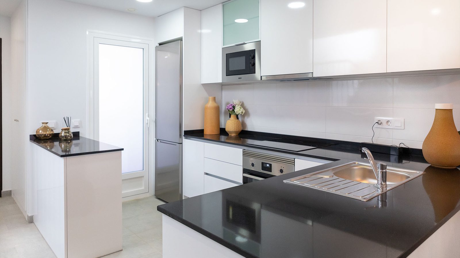 Modern white kitchen with black countertops, breakfast bar, integrated appliances and sink in a 2-bedroom bungalow in Pulpí - The Estates