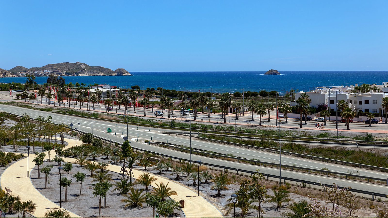 Sea and coastal resort view with palm-lined paths, roads and hillside across the bay from a 2-bedroom bungalow in Pulpí - The Estates