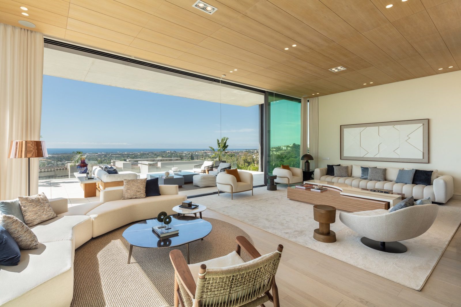 Modern living room with floor-to-ceiling windows, contemporary furnishings and panoramic sea views in La Quinta, Benahavís, Málaga - The Estates