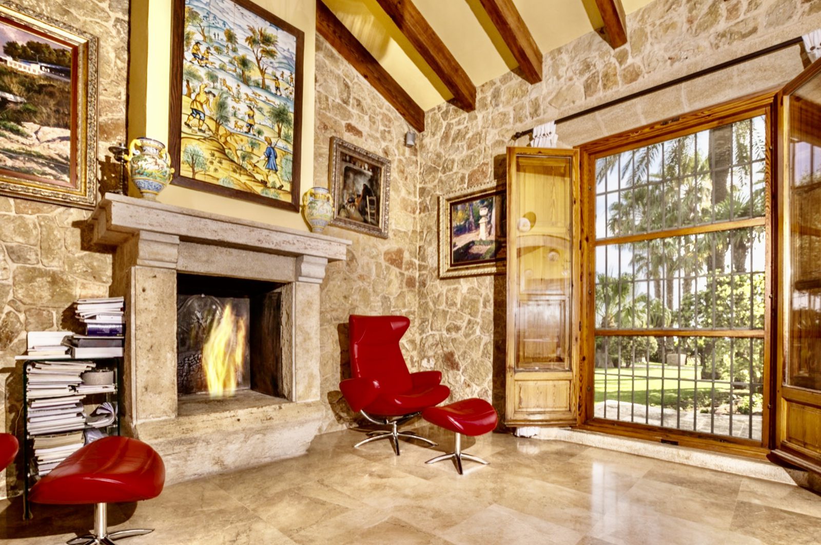 A cozy living room with a stone fireplace and large windows overlooking a garden in a 7-bedroom finca in Denia - The Estates