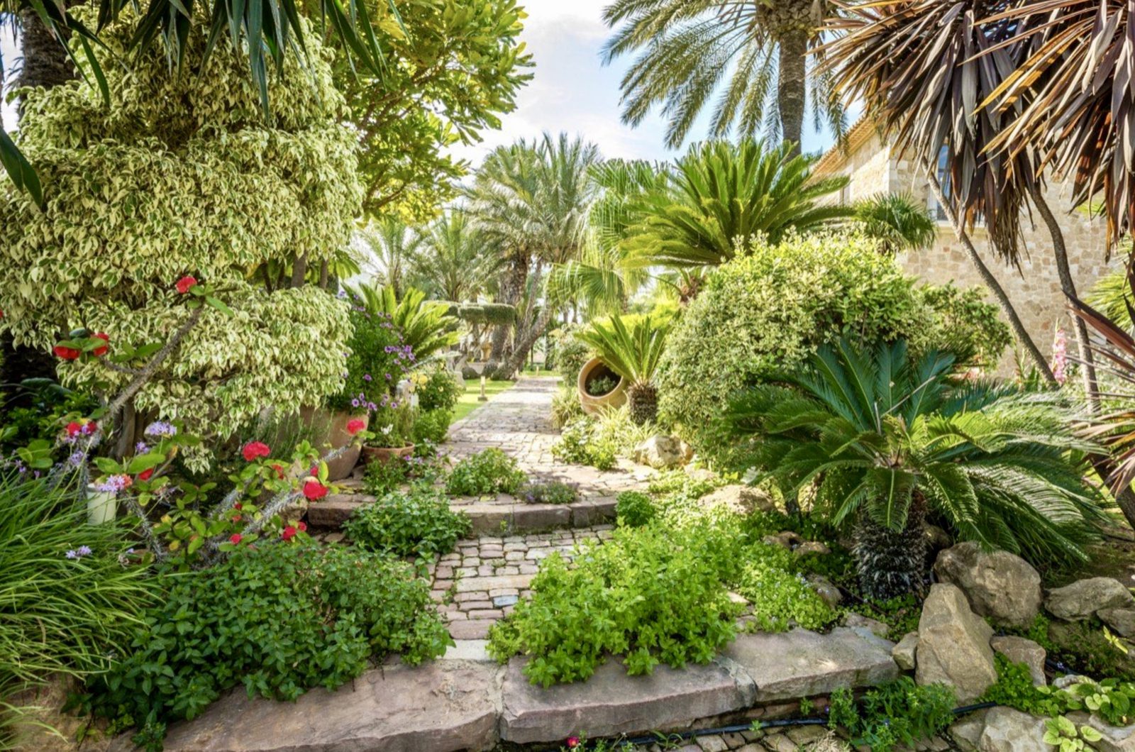 Lush garden with stone pathways and vibrant flowers surrounding a 7-bedroom finca in Denia - The Estates