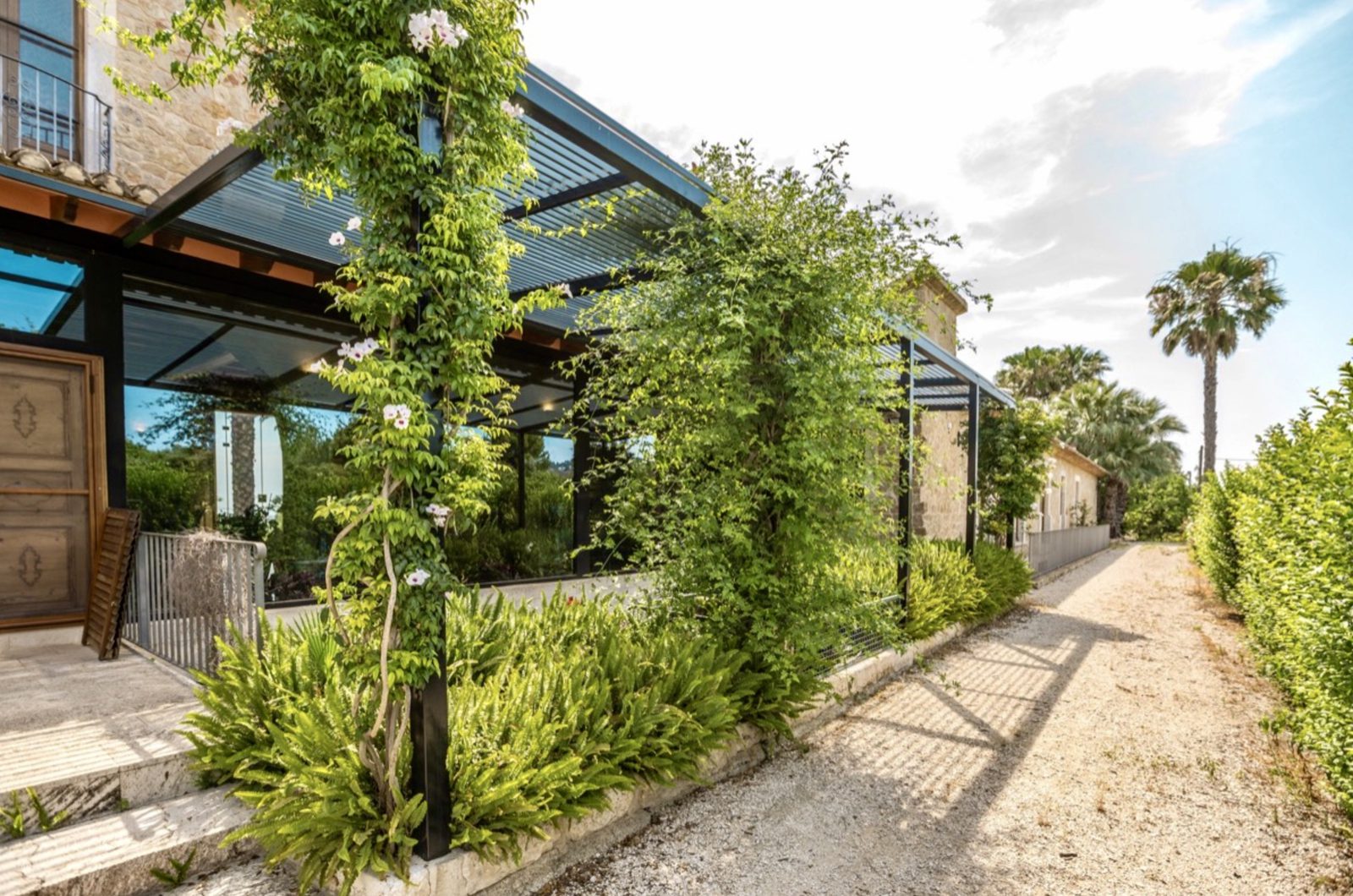 Exterior view of a stone finca with lush greenery and a covered terrace - The Estates