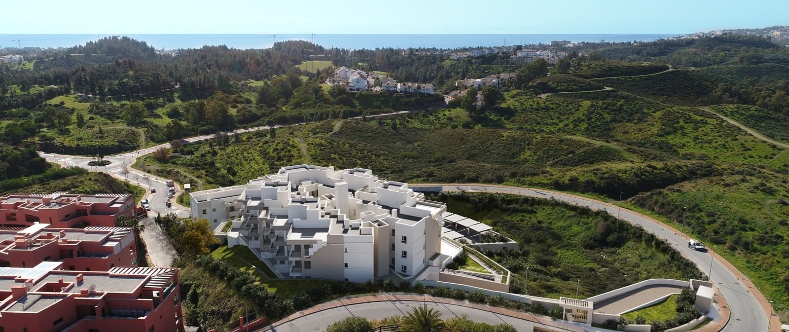 Aerial view of a white apartment complex, surrounding countryside and sea in Las Lagunas de Mijas, for a 2-bedroom apartment in Las Lagunas de Mijas - The Estates