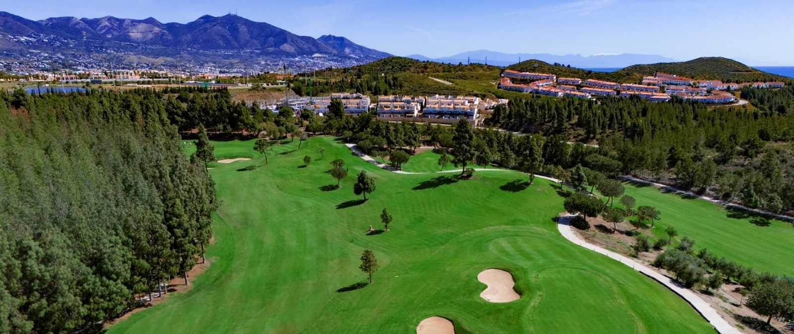 Aerial view of a golf course, surrounding residences, mountains and sea near a 2-bedroom apartment in