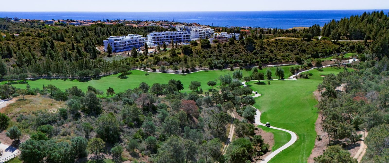 Aerial view of a golf course, apartment complex and Mediterranean Sea near a 2-bedroom apartment in Las Lagunas de Mijas - The Estates