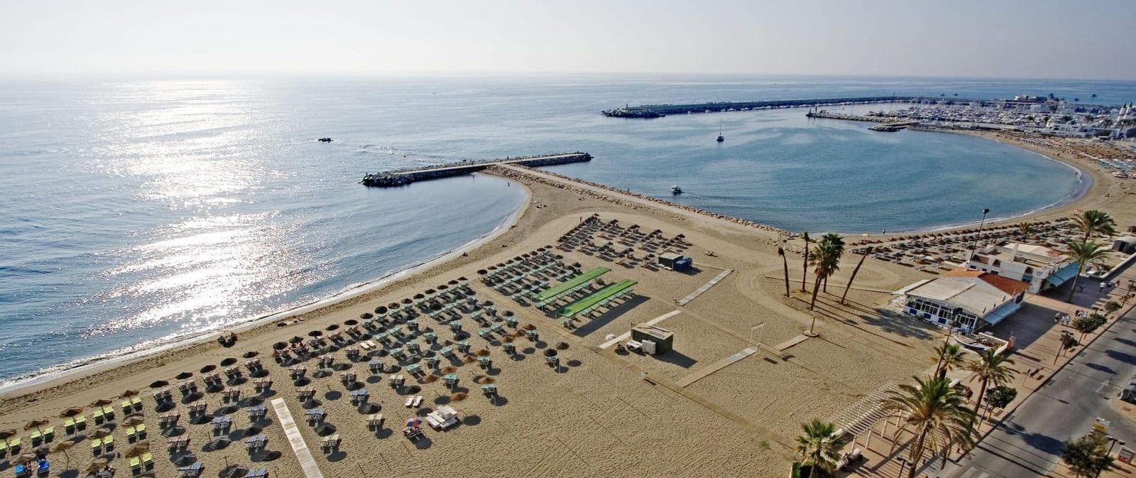 Aerial view of a sunny beach, marina and sheltered bay in Las Lagunas de Mijas - The Estates