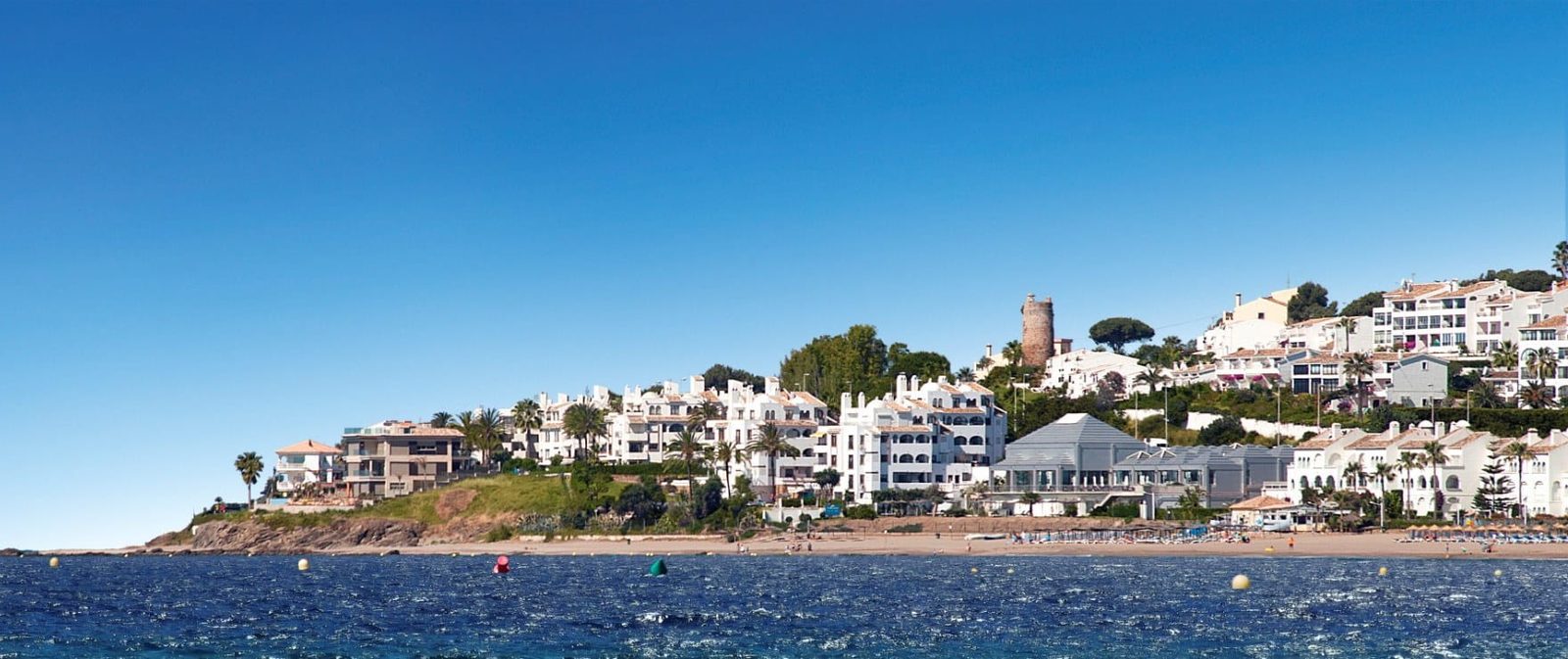 Coastal resort with a sandy beach, blue sea and white hillside buildings of a 2-bedroom apartment in Las Lagunas de Mijas - The Estates