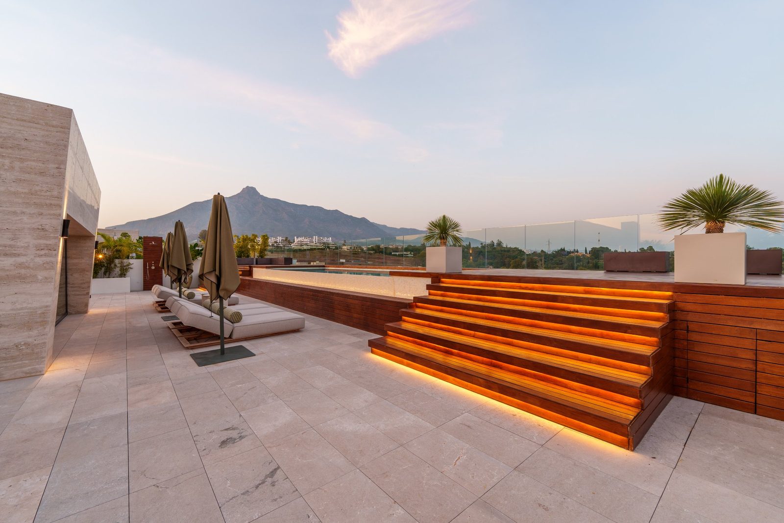 Rooftop terrace with pool, loungers and illuminated wooden steps overlooking mountain scenery in Marbella, Golden Mile, Málaga - The Estates