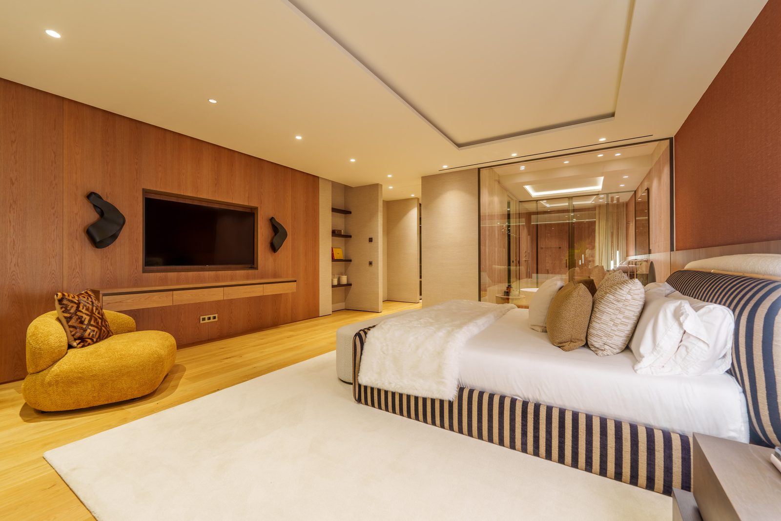 Contemporary master bedroom with wood-panelled TV wall, upholstered bed and seating in a 4-bedroom penthouse in Málaga - The Estates