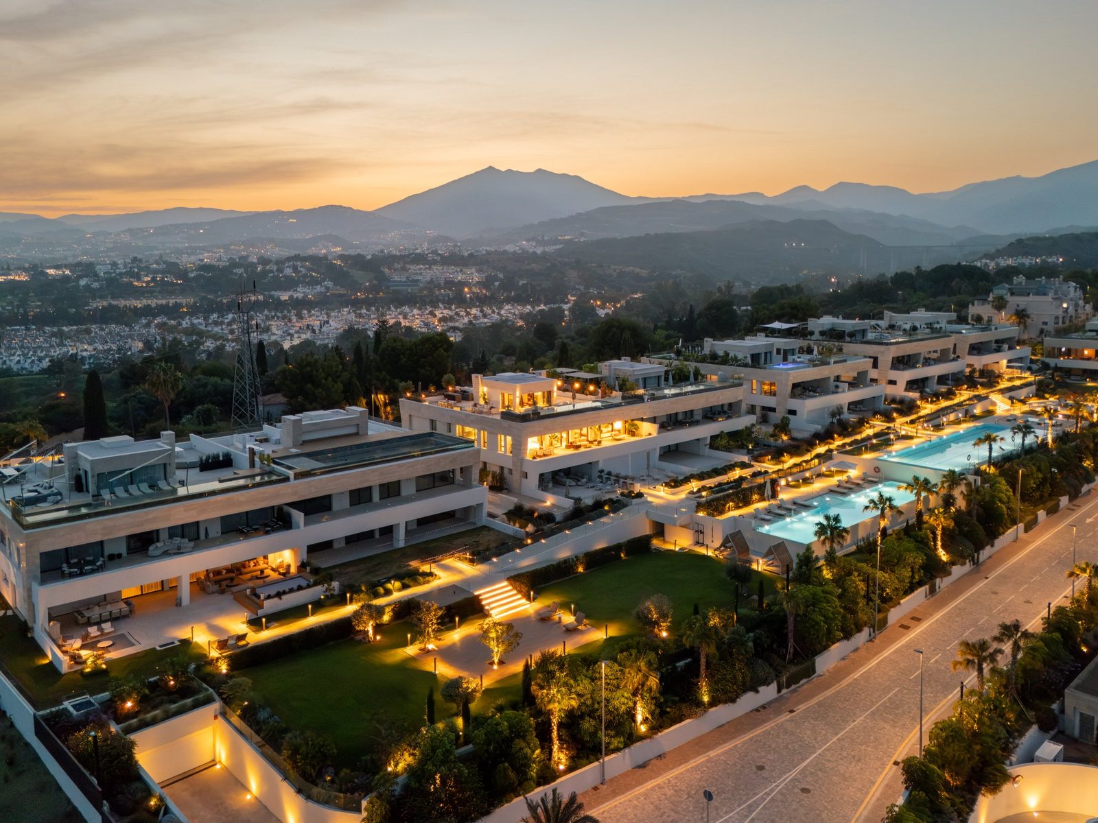 Aerial view of illuminated residences and pools at sunset, with