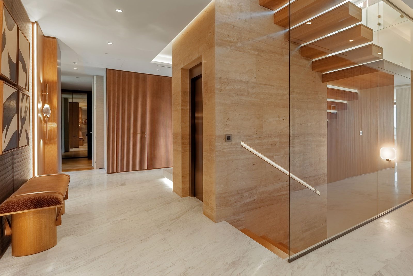 Elegant entrance hall with travertine walls, glass staircase and warm wood detailing of a 4