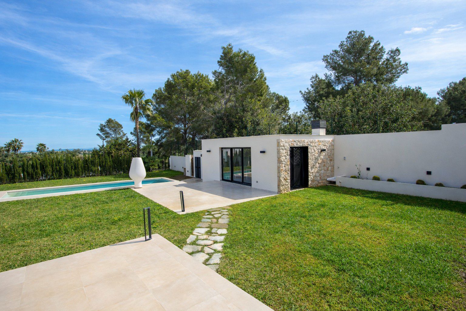 A modern villa with a pool and garden, set against a backdrop of countryside in Denia - The Estates